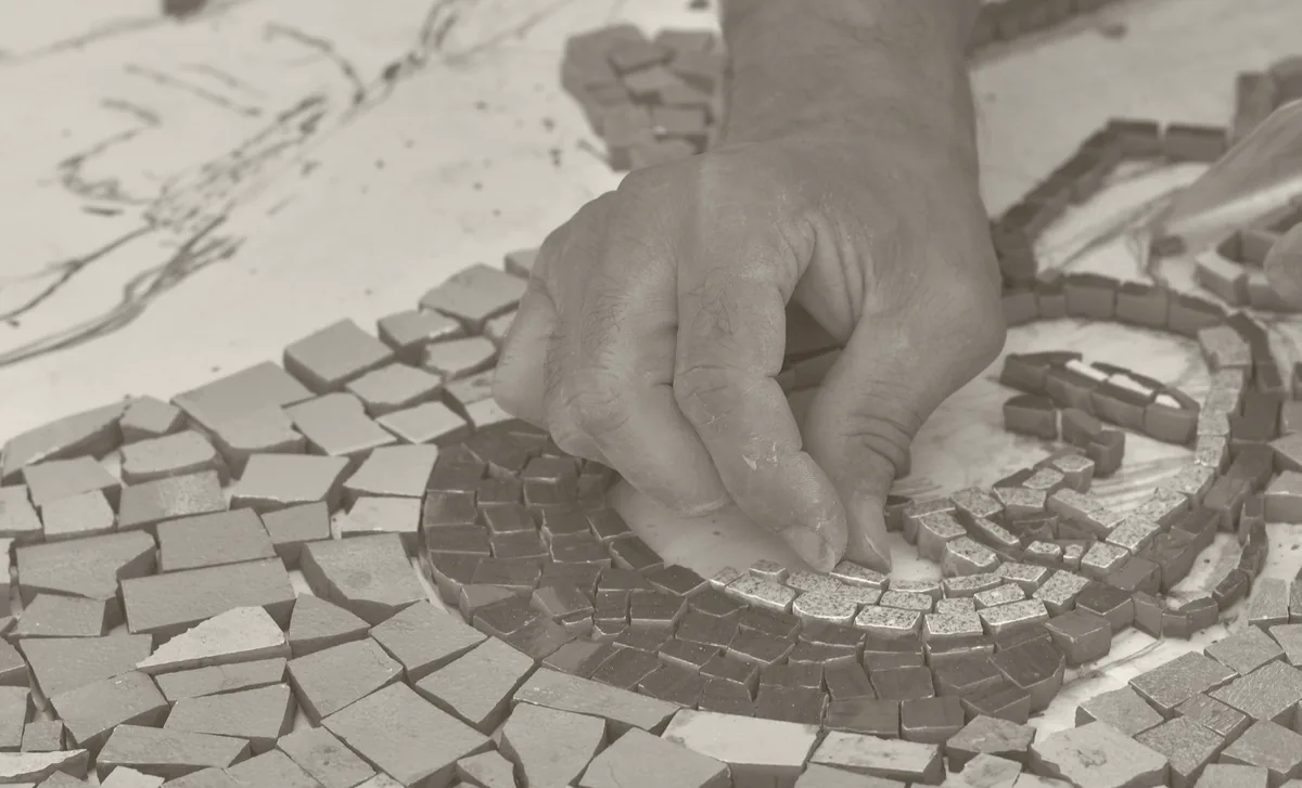 Una mano coloca un trozo de cerámica en un mosaico en construcción